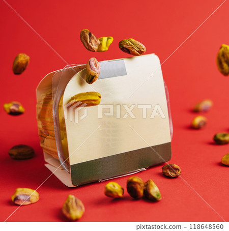 Pistachios falling from the sky onto packaging against red background 118648560