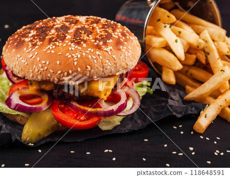 Delicious cheeseburger lying on black paper next to french fries Delicious cheeseburger lying on black paper next to french fries 118648591