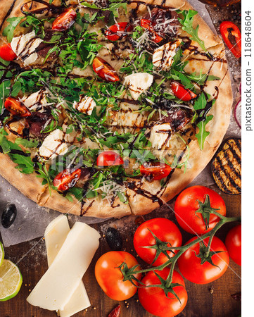 Freshly baked pizza lying on table with ingredients spread around 118648604