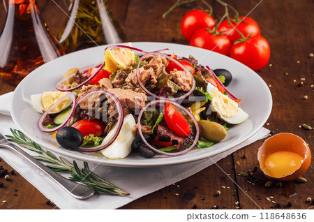 Fresh nicoise salad with tuna on a wooden table being prepared with eggs and tomatoes around Fresh nicoise salad with tuna on a wooden table being prepared with eggs and tomatoes around 118648636