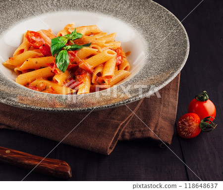 Penne pasta dish with tomato sauce and basil garnishing on wooden table 118648637