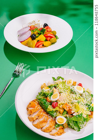 Caesar salad and greek salad on green background with fork resting nearby 118648755