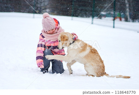 Little Girl And A Golden Retriever Puppy Playing In The Snow Outdoors In Winter, With The Dog Giving A Paw 118648770
