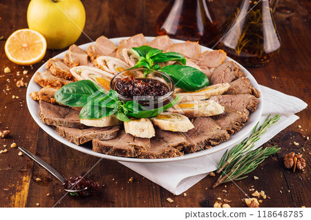Meat platter with sliced beef, chicken rolls, sauce and basil leaves on wooden table 118648785