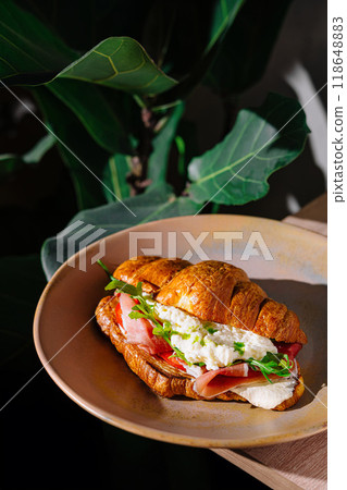 Delicious croissant sandwich with prosciutto, soft cheese and arugula on a plate Delicious croissant sandwich with prosciutto, soft cheese and arugula on a plate 118648883