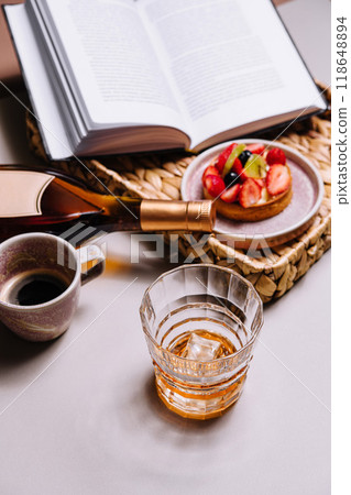 Glass of whisky with ice and bottle enjoying leisure time with book and dessert Glass of whisky with ice and bottle enjoying leisure time with book and dessert 118648894