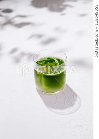 Green iced matcha latte standing on white table with leaf shadows 118649055
