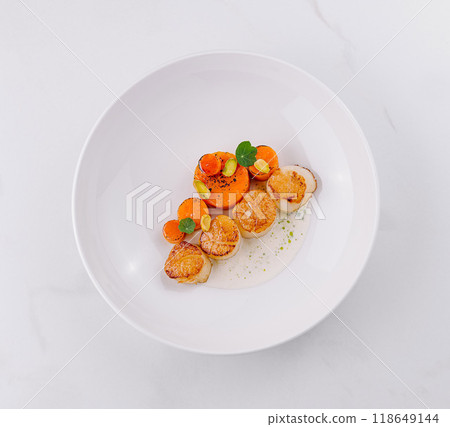 Seared scallops plate garnished with carrot and pistachio being served in a restaurant Seared scallops plate garnished with carrot and pistachio being served in a restaurant 118649144