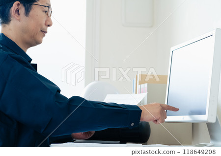 A man in work clothes comparing a computer and documents 118649208