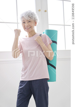 An elderly woman doing a fist pump while holding a yoga mat An elderly woman doing a fist pump while holding a yoga mat 118649598