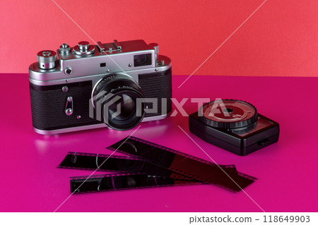 Vintage Film Camera with Exposure Meter and Negatives on a Pink Surface and Red Background Vintage Film Camera with Exposure Meter and Negatives on a Pink Surface and Red Background 118649903