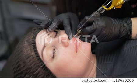 Permanent makeup. The master makes a lip tattoo for a client in a beauty salon. Young woman undergoing procedure of permanent lip makeup in tattoo salon, closeup. 118650200
