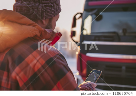 The truck driver checks a tracking app on his smartphone beside his truck 118650764