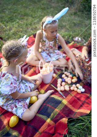 two little girls and mom paint eggs at easter picnic 118650794
