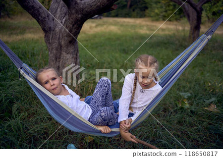 little sisters girls playing together in a hammock, camping with the children little sisters girls playing together in a hammock, camping with the children 118650817