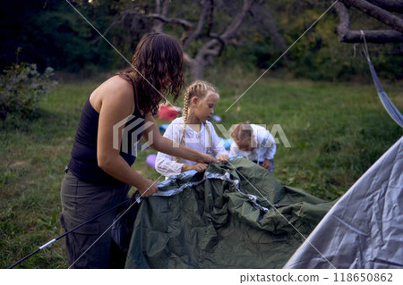 mother and little daughters are setting up a tourist tent in  forest, camping with children 118650862