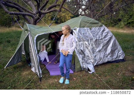 mother and little daughters are setting up a tourist tent in forest, camping with children mother and little daughters are setting up a tourist tent in forest, camping with children 118650872