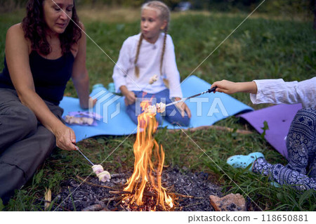 mother and her daughters roasting and eating marshmallows on the campfire, camping vacation with children, mosquito bites on children's faces mother and her daughters roasting and eating marshmallows on the campfire, camping vacation with children, mosquito bites on children's faces 118650881