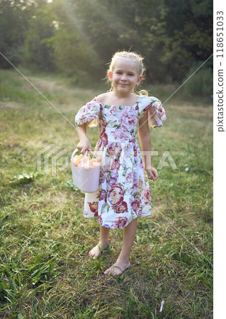 little blond girl with braids in a floral dress with a basket on an Easter egg hunt little blond girl with braids in a floral dress with a basket on an Easter egg hunt 118651033