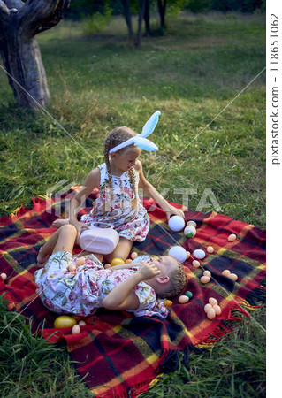 little girls, sisters, playing on a picnic blanket with eggs after an Easter egg hunt little girls, sisters, playing on a picnic blanket with eggs after an Easter egg hunt 118651062