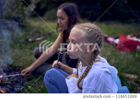 mother and her daughters  roasting and eating marshmallows on the campfire, camping vacation with children, mosquito bites on children's faces 118651089