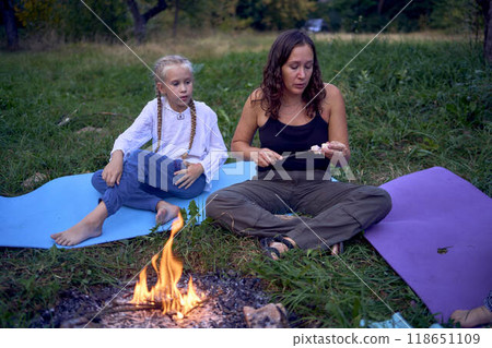 mother and her daughters  roasting and eating marshmallows on the campfire, camping vacation with children, mosquito bites on children's faces 118651109
