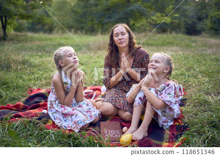 a mother and her two daughters read the holy bible and pray at an Easter picnic 118651346