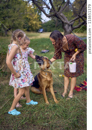mom and little girls sisters playing with german shepherd dog during easter picnic in the garden 118651379