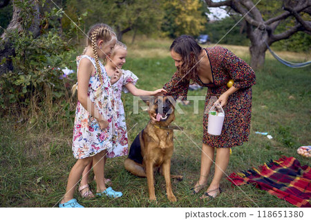 mom and little girls sisters playing with german shepherd dog during easter picnic in the garden 118651380