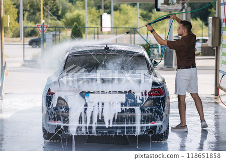 Man washes off the foam from the car with water under high pressure Man washes off the foam from the car with water under high pressure 118651858
