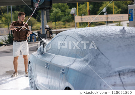 Cleaning car using active foam. Handsome man washing his luxury car on self car-washing Cleaning car using active foam. Handsome man washing his luxury car on self car-washing 118651890