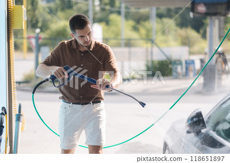 Young man cleaning car using high pressure water on self-service car wash.  118651897