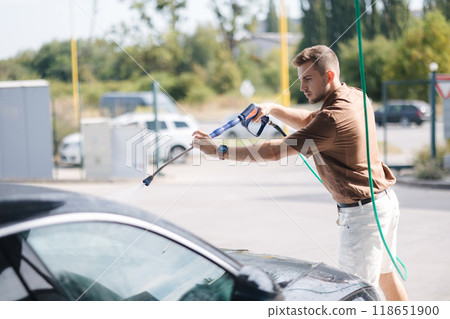 Young man cleaning car using high pressure water on self-service car wash. Young man cleaning car using high pressure water on self-service car wash. 118651900