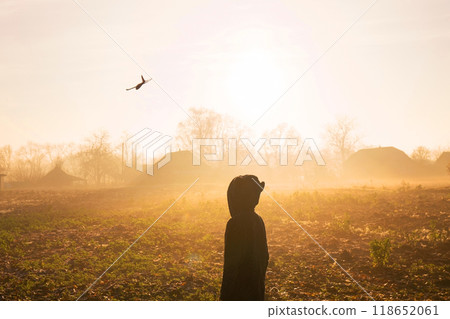 A boy launches an airplane on a foggy sunny morning. Photo from the back 118652061