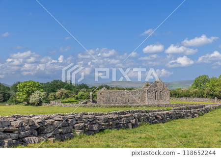 Stone ruins of Kilmacduagh Abbey surrounded by stone wall and green fields under blue sky in Ireland Stone ruins of Kilmacduagh Abbey surrounded by stone wall and green fields under blue sky in Ireland 118652244