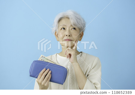A senior woman pondering while looking at the money in her wallet A senior woman pondering while looking at the money in her wallet 118652389