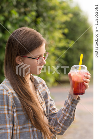 A teenage girl in glasses drinks bubble tea on a walk 118652661