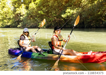 Two young women floating and smiling in a kayak on the river.  118654373