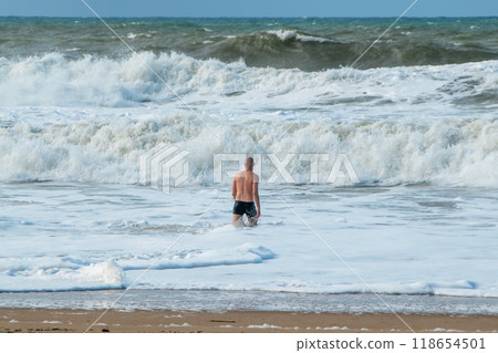 A man alone swims in the Atlantic Ocean in a storm, big waves, danger on the beach A man alone swims in the Atlantic Ocean in a storm, big waves, danger on the beach 118654501