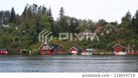 Small  red boat sheds and cottages at the shore of the Tengs River, Egersund, Norway. 118654719