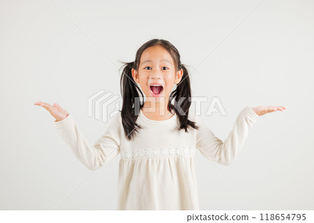 A jubilant kid girl raises her fists in celebration of her success, saying yes with excitement. Asian portrait of a happy young kindergarten child in a studio shot on a white background, winning 118654795