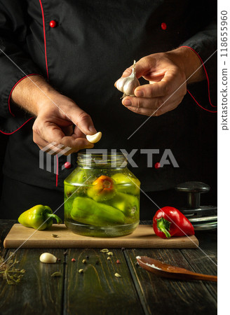 A chef adds garlic to bell pepper before canning them in a jar. Pickling peppers with aromatic spices on the kitchen counter. Advertising space on the black table A chef adds garlic to bell pepper before canning them in a jar. Pickling peppers with aromatic spices on the kitchen counter. Advertising space on the black table 118655960