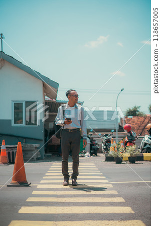 A man walks confidently through a busy crosswalk, checking his phone 118657005