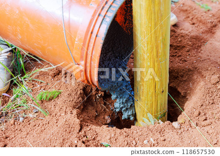 Pouring concrete on newly installed timber fencing wooden fence posts 118657530