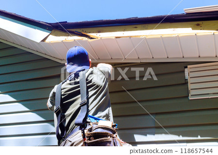 As construction process, an employee installs vinyl plastic siding panels on wall facade of new home As construction process, an employee installs vinyl plastic siding panels on wall facade of new home 118657544