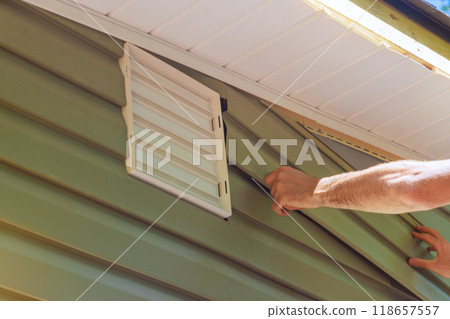 Construction employee installs vinyl plastic siding panels on facade of new house during construction 118657557