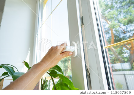 The hand holds the handle of a plastic double-glazed window, closing and opening the window with a rotary mechanism, the position of the handle for ventilation, micro-ventilation 118657869