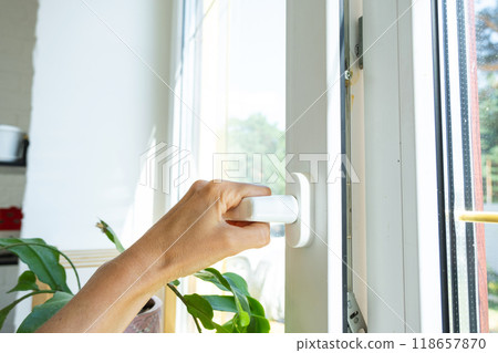 The hand holds the handle of a plastic double-glazed window, closing and opening the window with a rotary mechanism, the position of the handle for ventilation, micro-ventilation The hand holds the handle of a plastic double-glazed window, closing and opening the window with a rotary mechanism, the position of the handle for ventilation, micro-ventilation 118657870