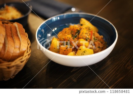 yellow food in a blue plate. vegetable stew with potatoes carrots pepper sprinkled with herbs. High quality photo food on a wooden table. The view of the food is shot at 45 degrees. There is also yellow food in a blue plate. vegetable stew with potatoes carrots pepper sprinkled with herbs. High quality photo food on a wooden table. The view of the food is shot at 45 degrees. There is also 118658481
