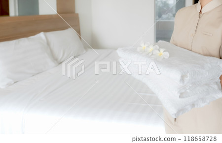 Hands of hotel maid putting plumeria flower and towels on the bed in the luxury hotel room ready for tourist travel 118658728